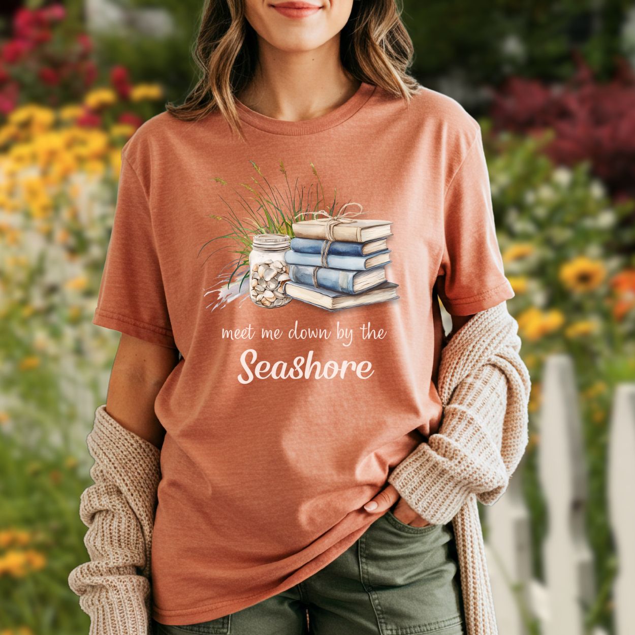 Garment-dyed peach t-shirt with "Meet Me Down By the Seashore" text and beach book graphic.