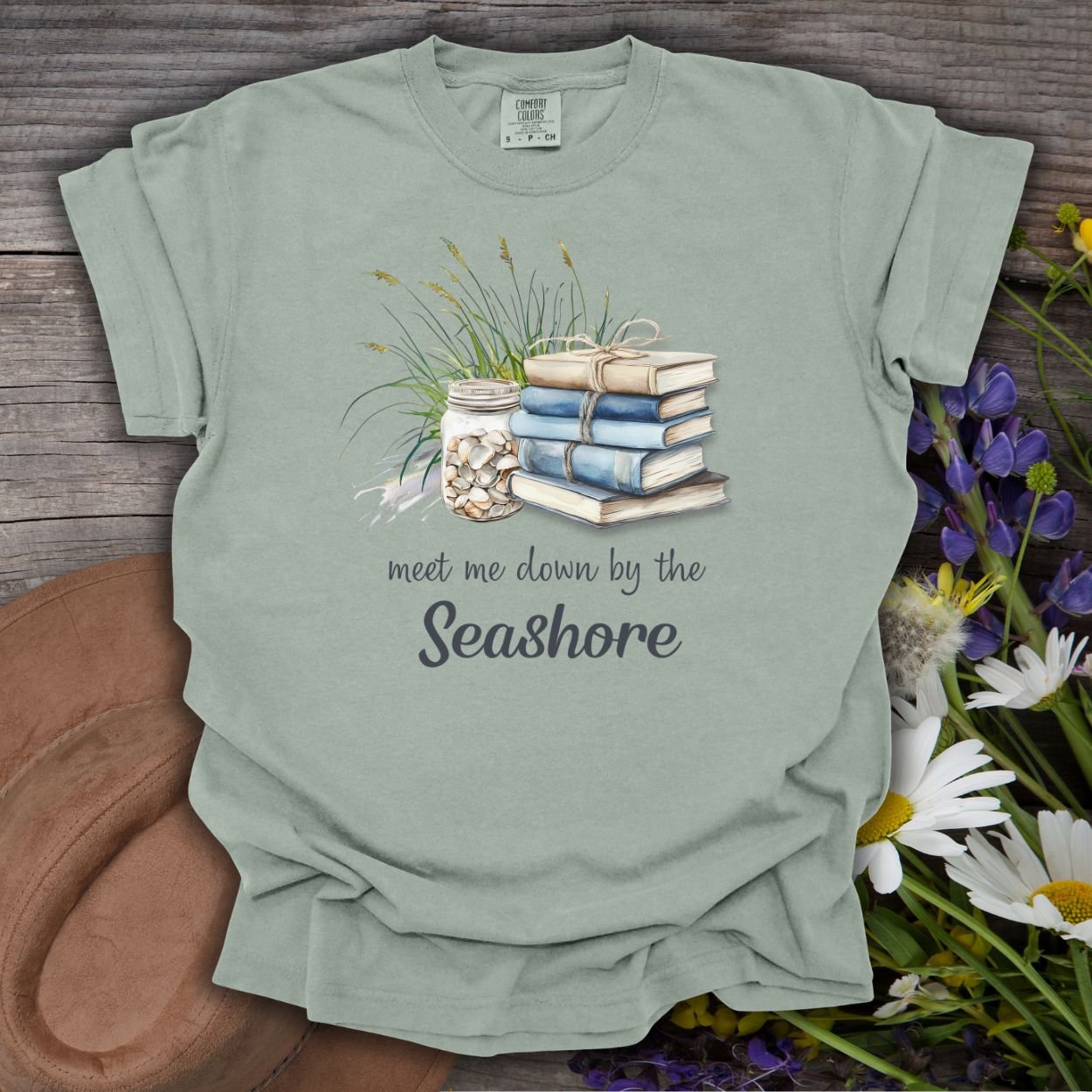Bay S garment-dyed t-shirt with "Meet Me Down By the Seashore" text, books, shells, and dune grass.
