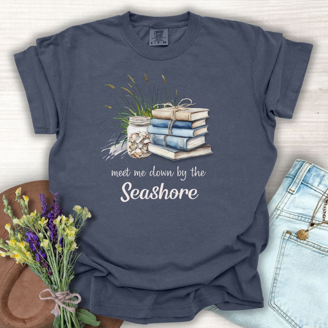 Denim S t-shirt with "meet me down by the Seashore" text, books, shells, and dune grass graphic.