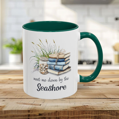 White ceramic 11oz mug with green handle and interior, featuring watercolor stacked books, beach grasses, shells, and "meet me down by the Seashore" text.