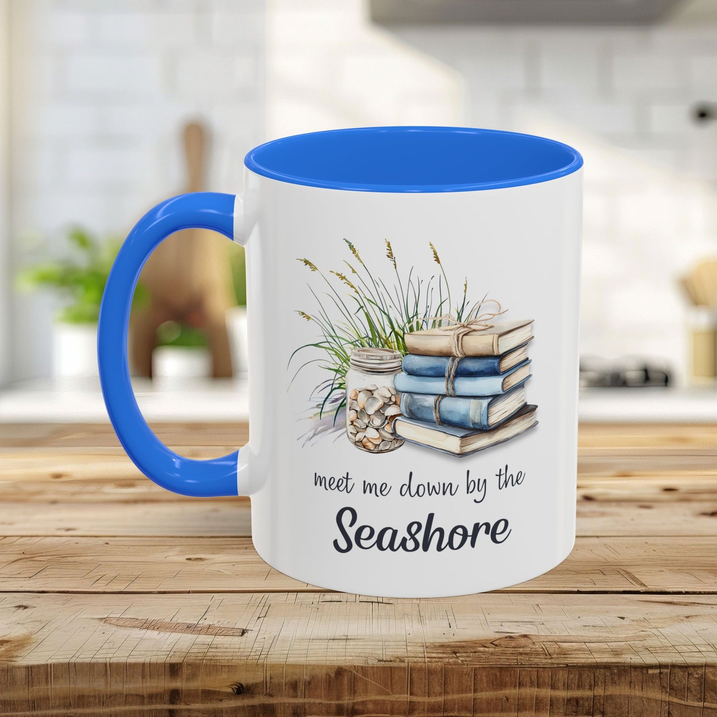 White ceramic mug with blue interior and handle, featuring watercolor art of stacked books, beach grasses, shells, and "meet me down by the Seashore.