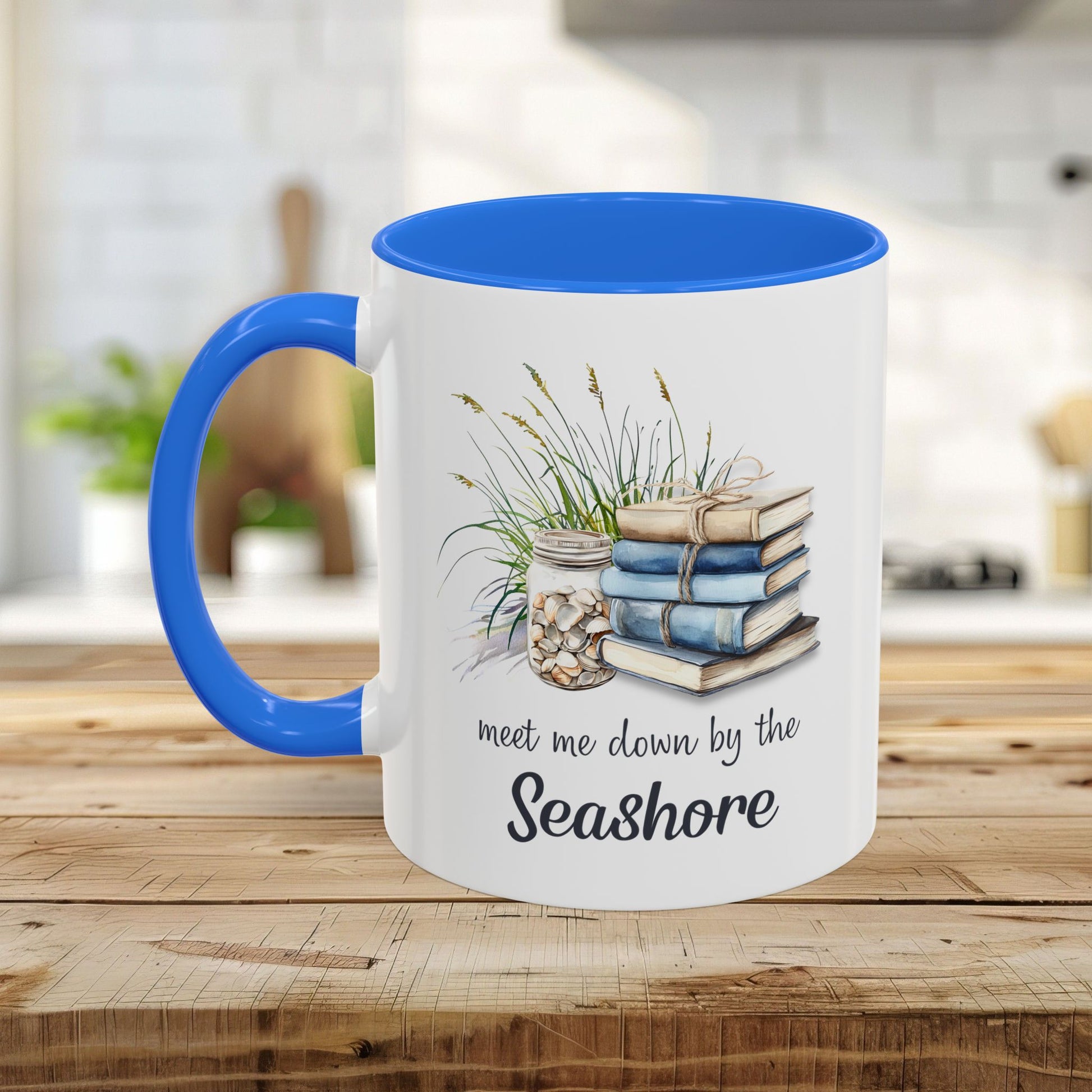 White ceramic mug with blue interior and handle, featuring watercolor art of stacked books, beach grasses, shells, and "meet me down by the Seashore.