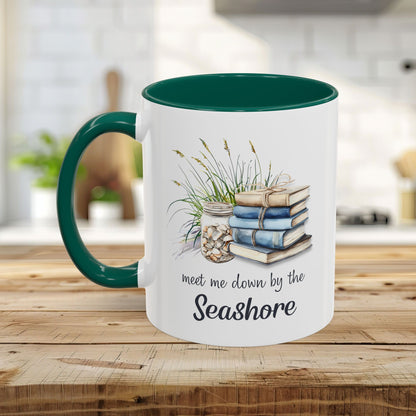 White ceramic mug with green handle and interior, featuring watercolor stacked books, beach grasses, shells, and "meet me down by the Seashore" text.