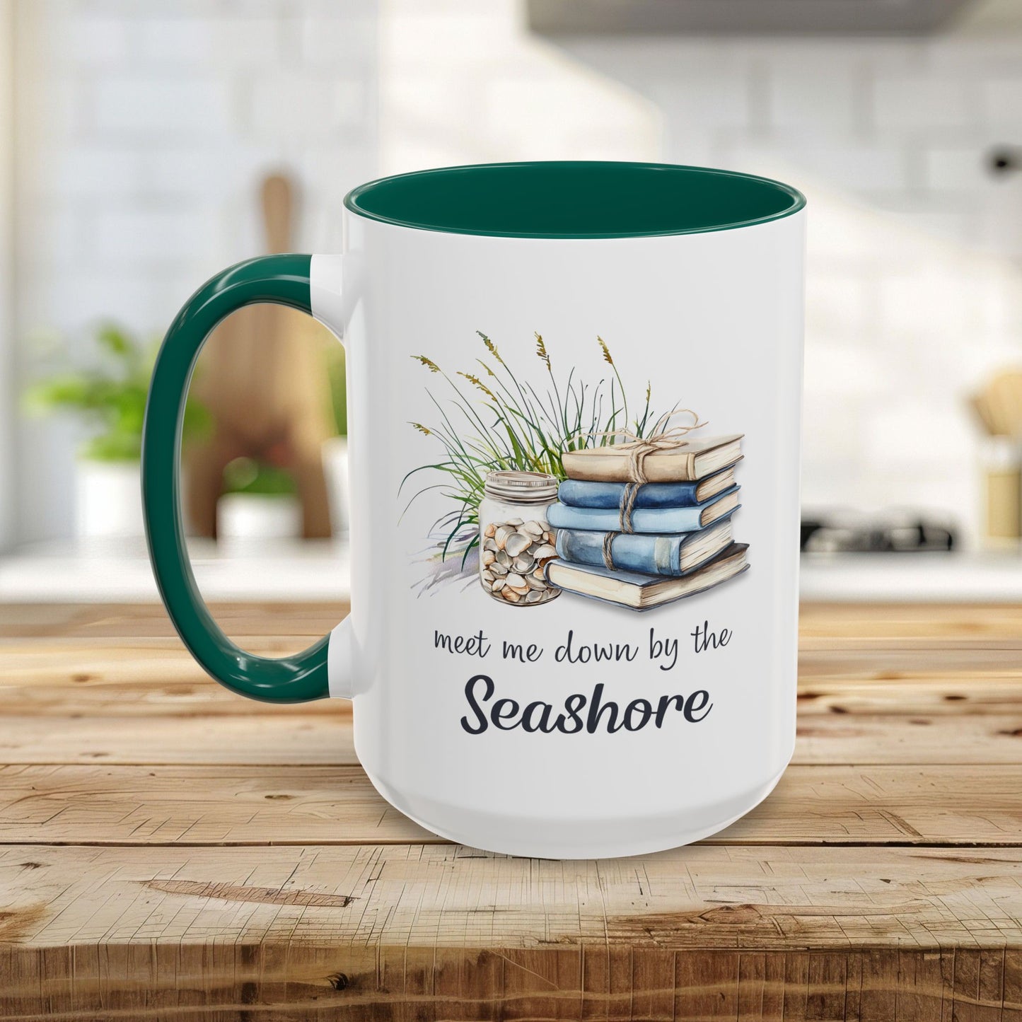 White ceramic mug with a dark green handle and interior, featuring watercolor art of stacked books, beach grasses, and shells.