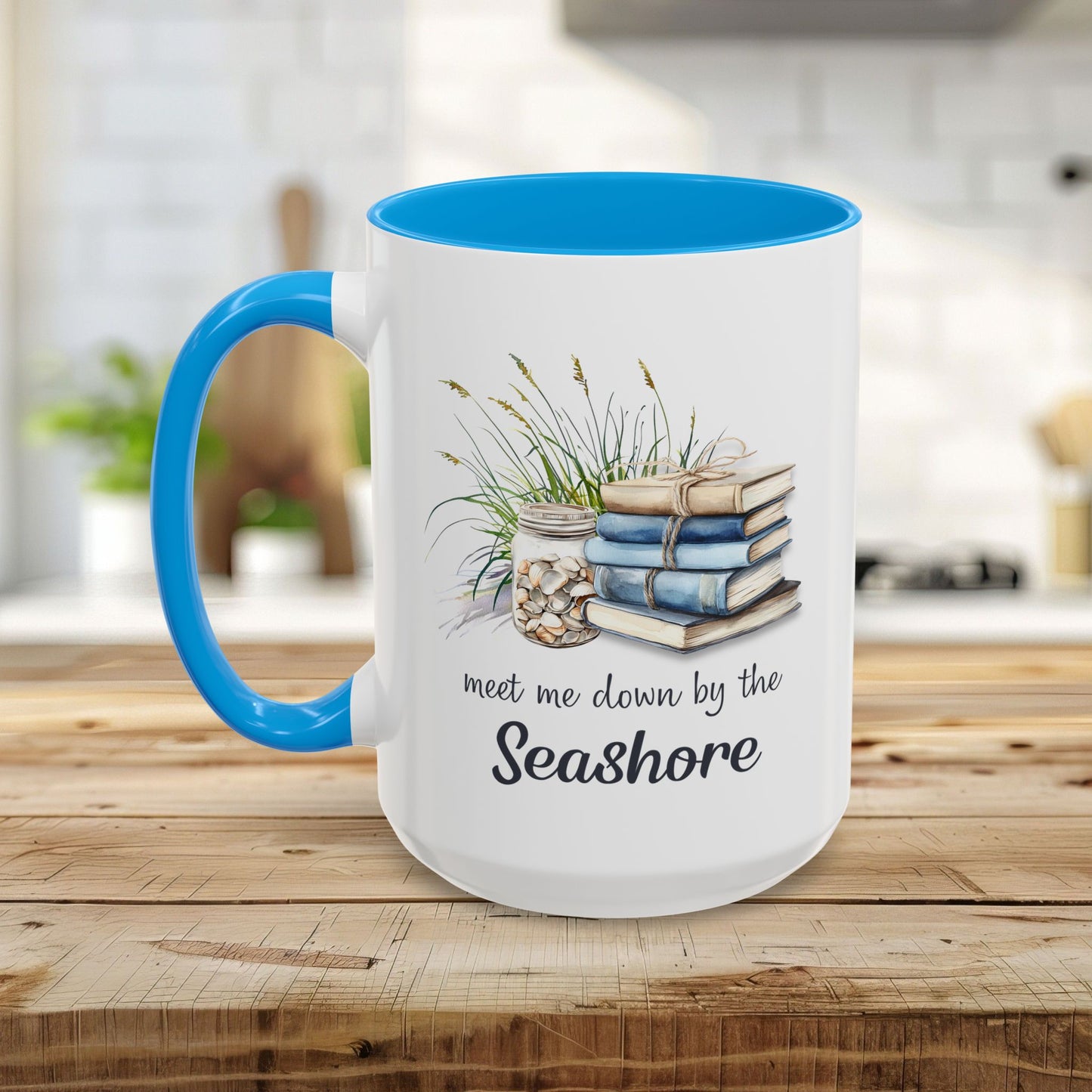 White ceramic mug with blue handle and interior, featuring watercolor art of stacked books, beach grasses, shells, and "meet me down by the Seashore.