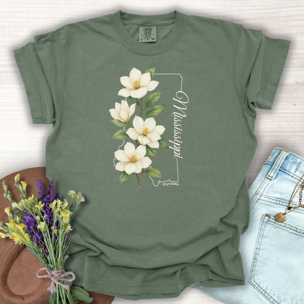 Moss green relaxed-fit t-shirt with a white magnolia illustration and Mississippi state outline.