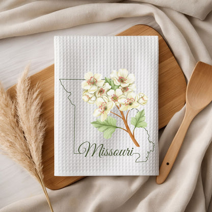 White microfiber tea towel with a hawthorn branch, Missouri outline, and "Missouri" script, on a wooden board.