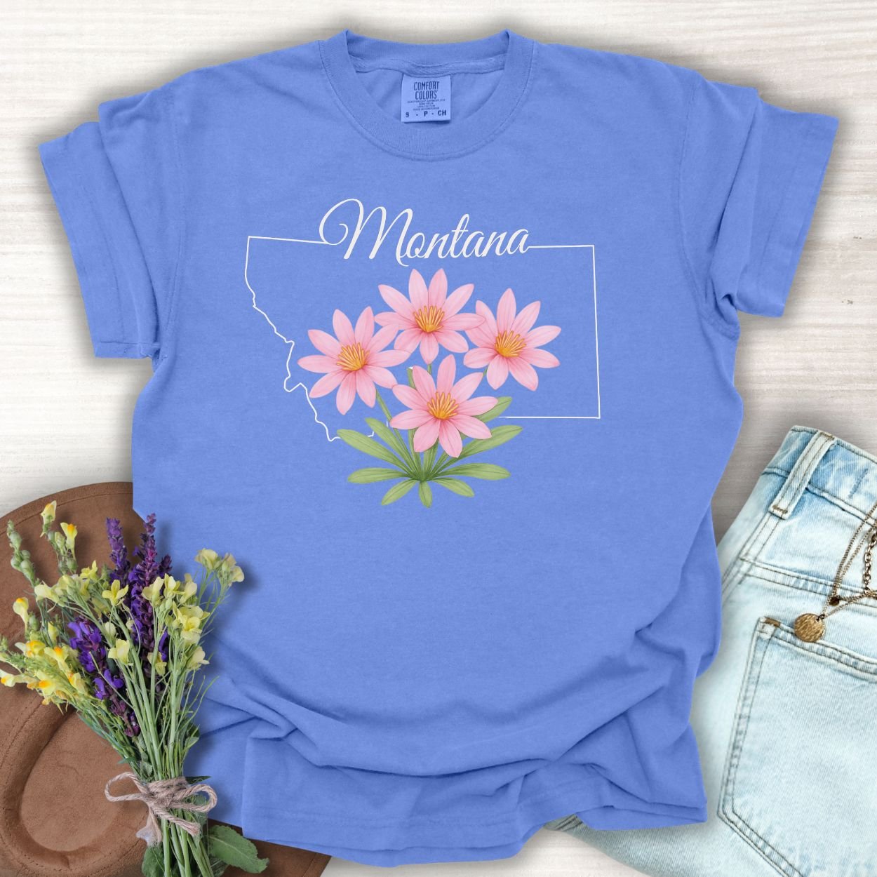 Periwinkle S t-shirt with a Montana outline and pink Bitterroot wildflowers.