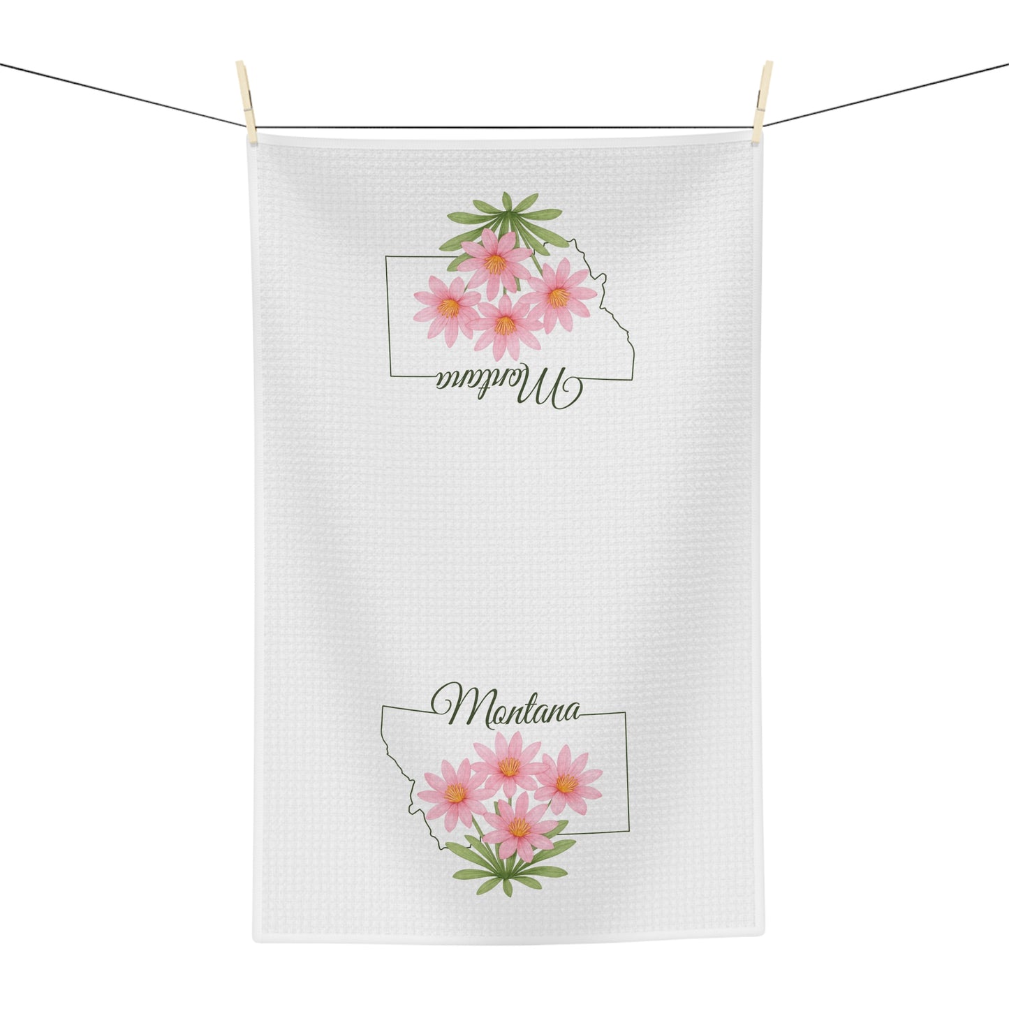 White microfiber tea towel with Montana outline and pink bitterroot flowers, hanging on a clothesline.