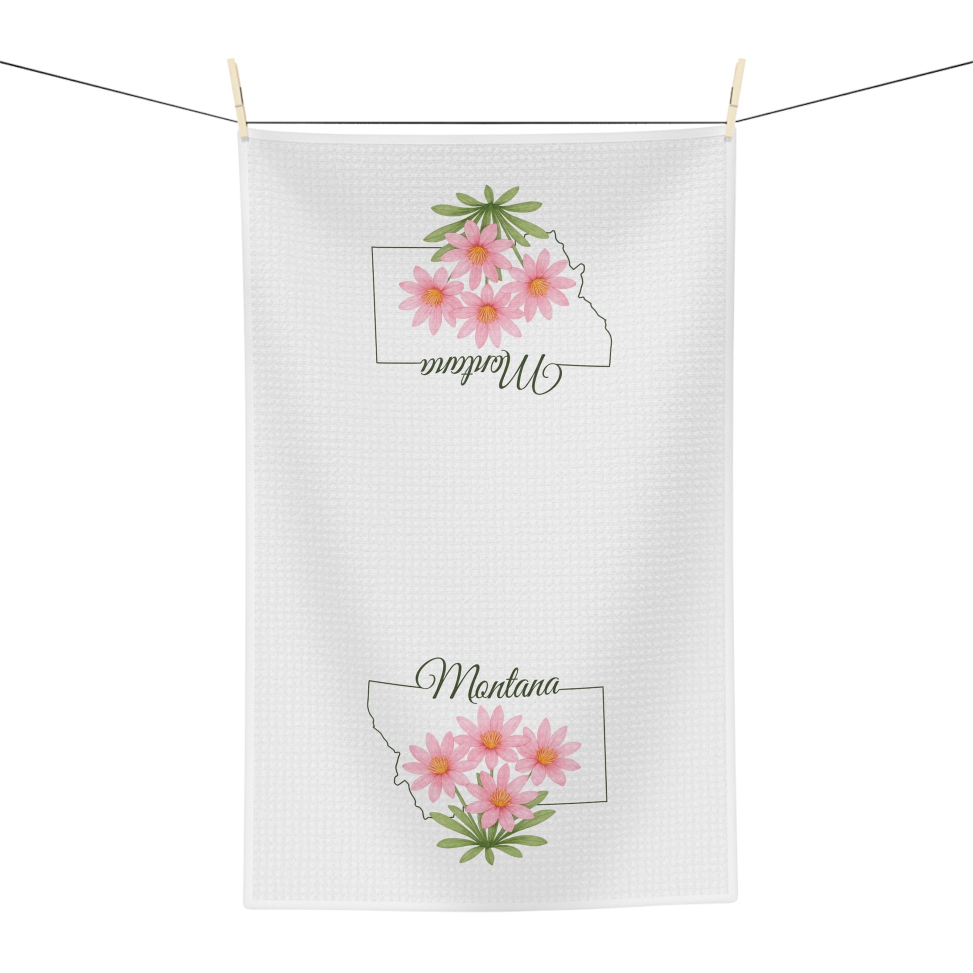 White microfiber tea towel with Montana outline and pink bitterroot flowers, hanging on a clothesline.