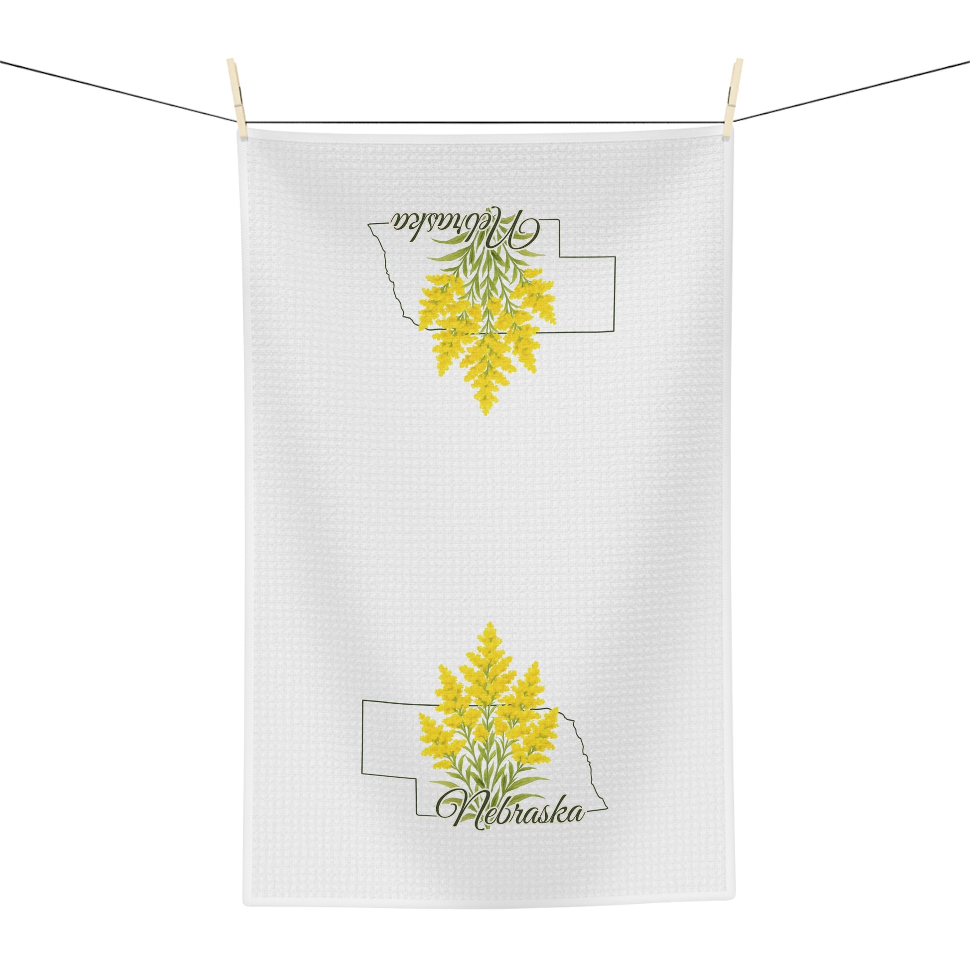 White microfiber tea towel with goldenrod flowers inside a Nebraska outline, hanging on a line.