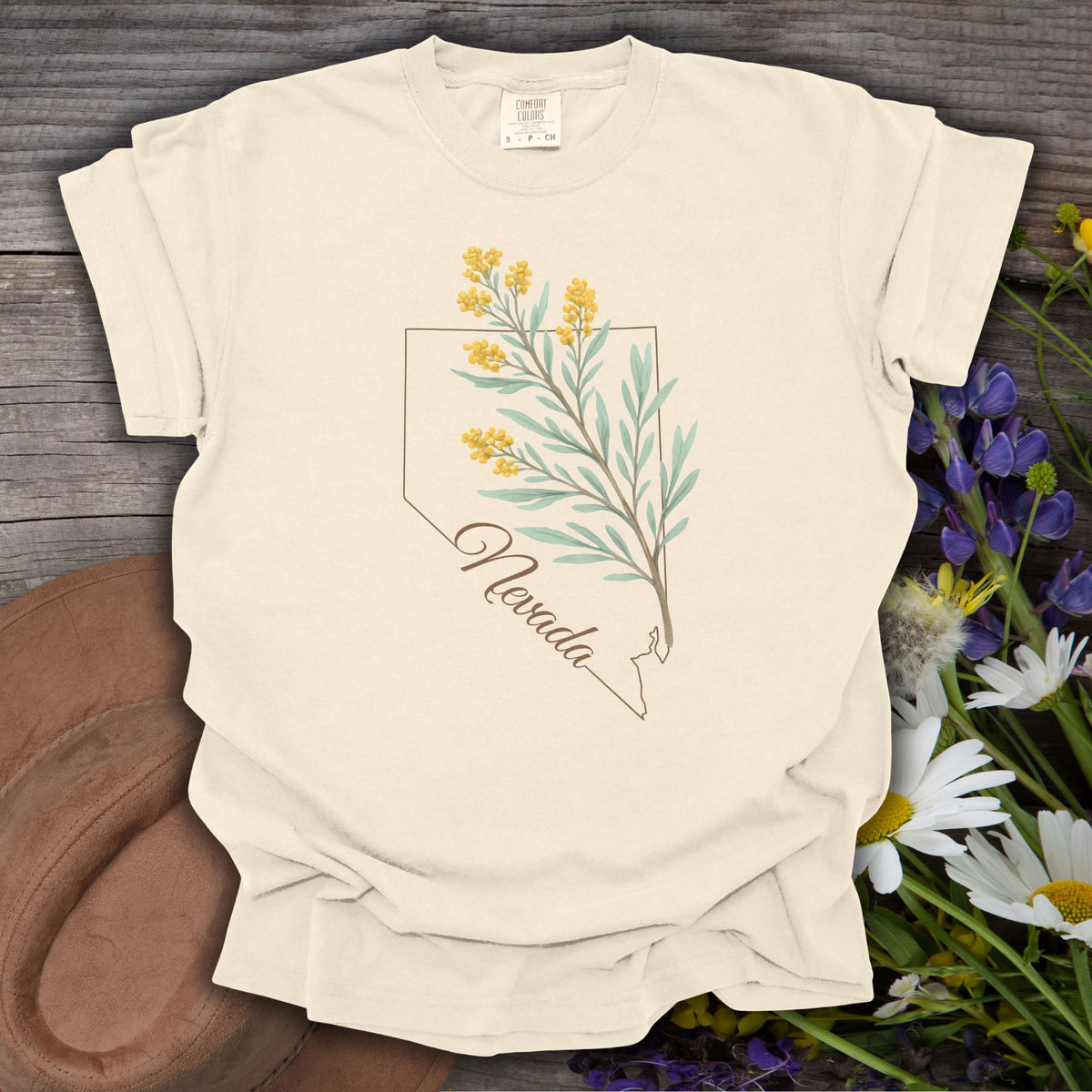 Ivory S-size Nevada floral state flower t-shirt with sagebrush design, laid on rustic wood with wildflowers.