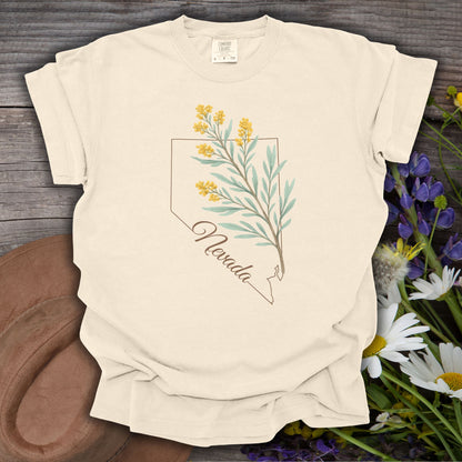 Ivory S-size Nevada floral state flower t-shirt with sagebrush design, laid on rustic wood with wildflowers.