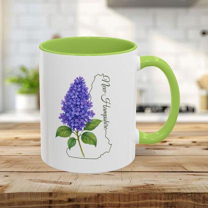 White 11oz ceramic mug with a light green interior and handle, featuring a vibrant lilac print and New Hampshire outline.