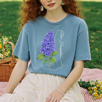 Woman in a relaxed-fit, garment-dyed blue t-shirt with a watercolor lilac and New Hampshire outline.