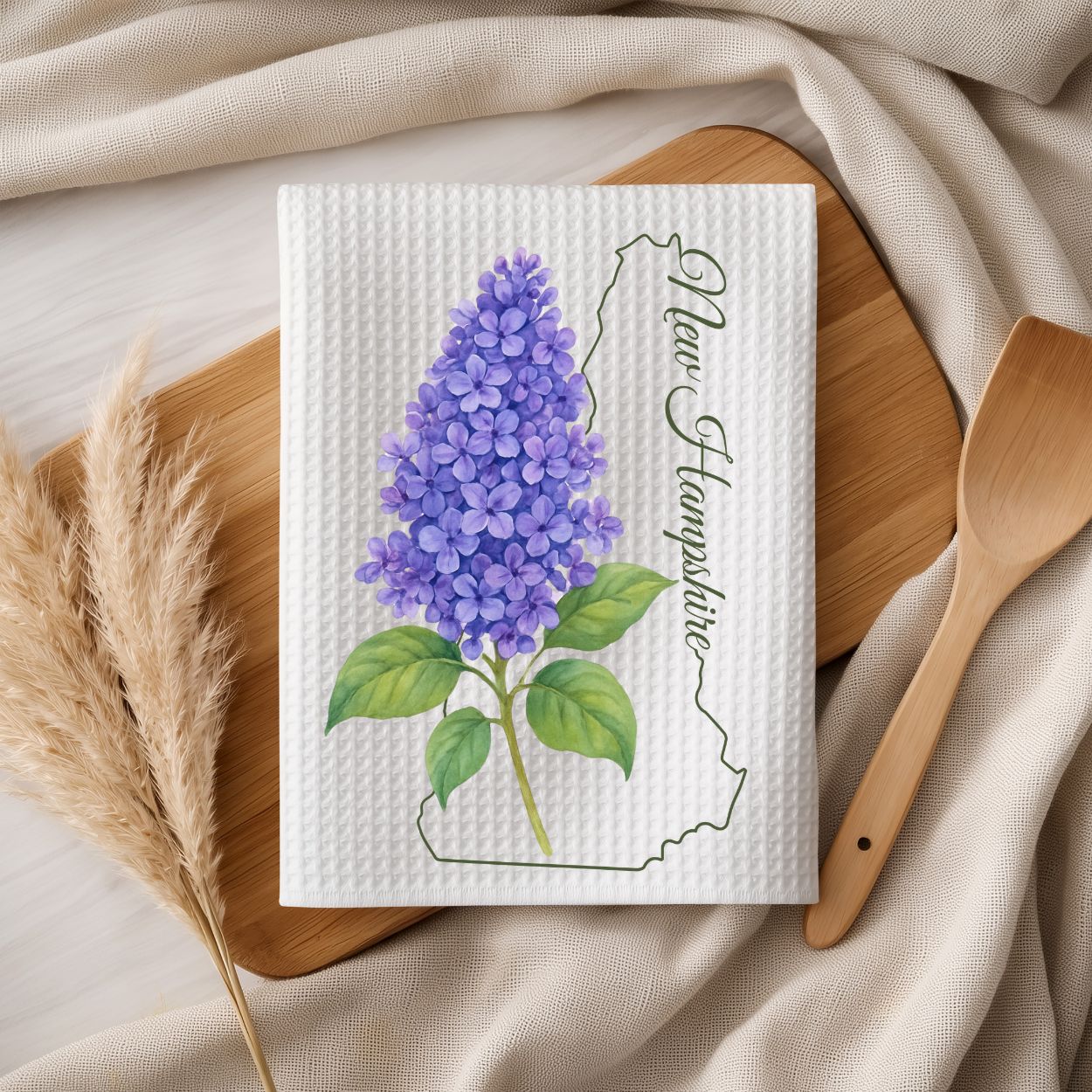 White microfiber tea towel with purple lilac sprigs, New Hampshire outline, and handwritten state name.
