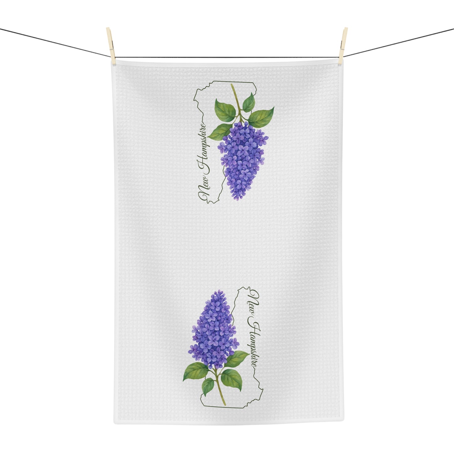 White microfiber tea towel with two purple lilac sprigs and "New Hampshire" text, hanging on a line.