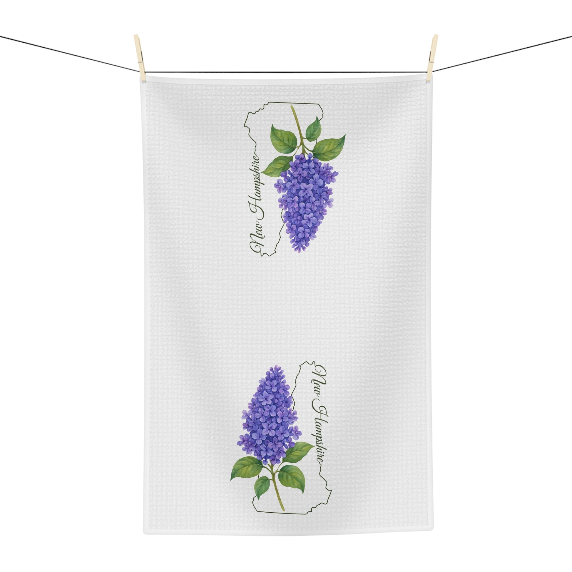 White microfiber tea towel with two purple lilac sprigs and "New Hampshire" text, hanging on a line.