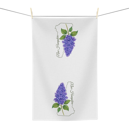 White microfiber tea towel with two purple lilac sprigs and "New Hampshire" text, hanging on a line.
