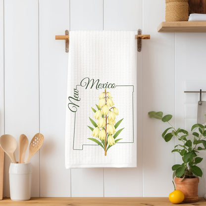 White microfiber tea towel with "New Mexico" and a yucca flower design, hanging on a wooden rack.