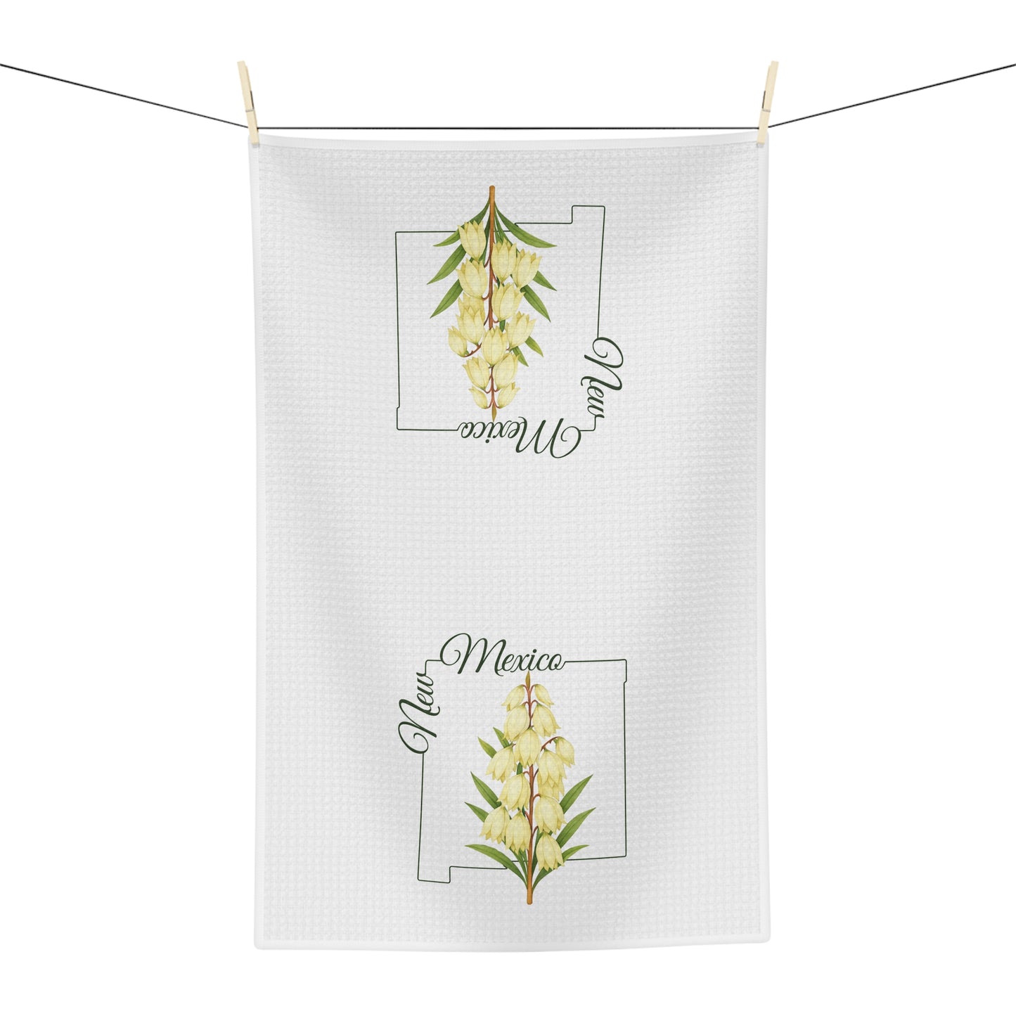 White microfiber tea towel with a watercolor yucca bloom and "New Mexico" text, hanging on a clothesline.