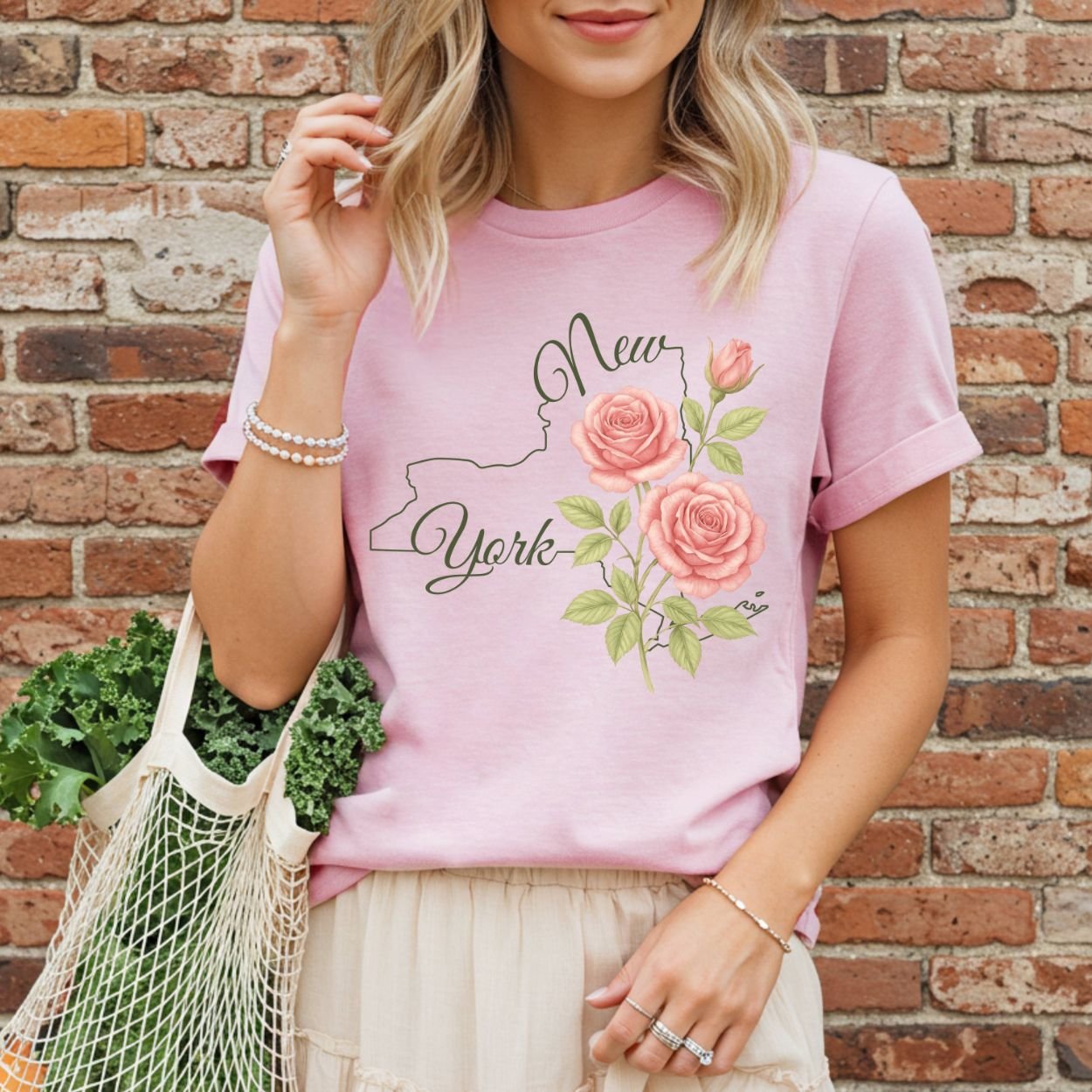 Woman in a relaxed-fit, garment-dyed pink cotton t-shirt with a New York state outline and painterly roses.