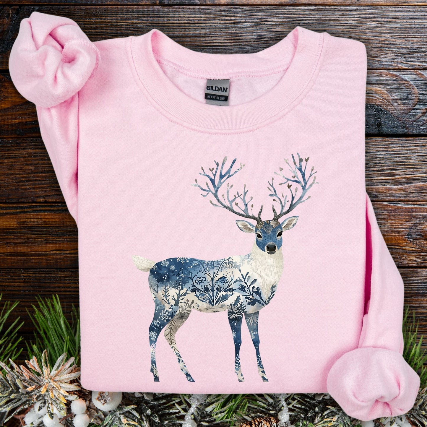 Light pink Gildan sweatshirt with a whimsical deer illustration featuring blue botanical and frost patterns.