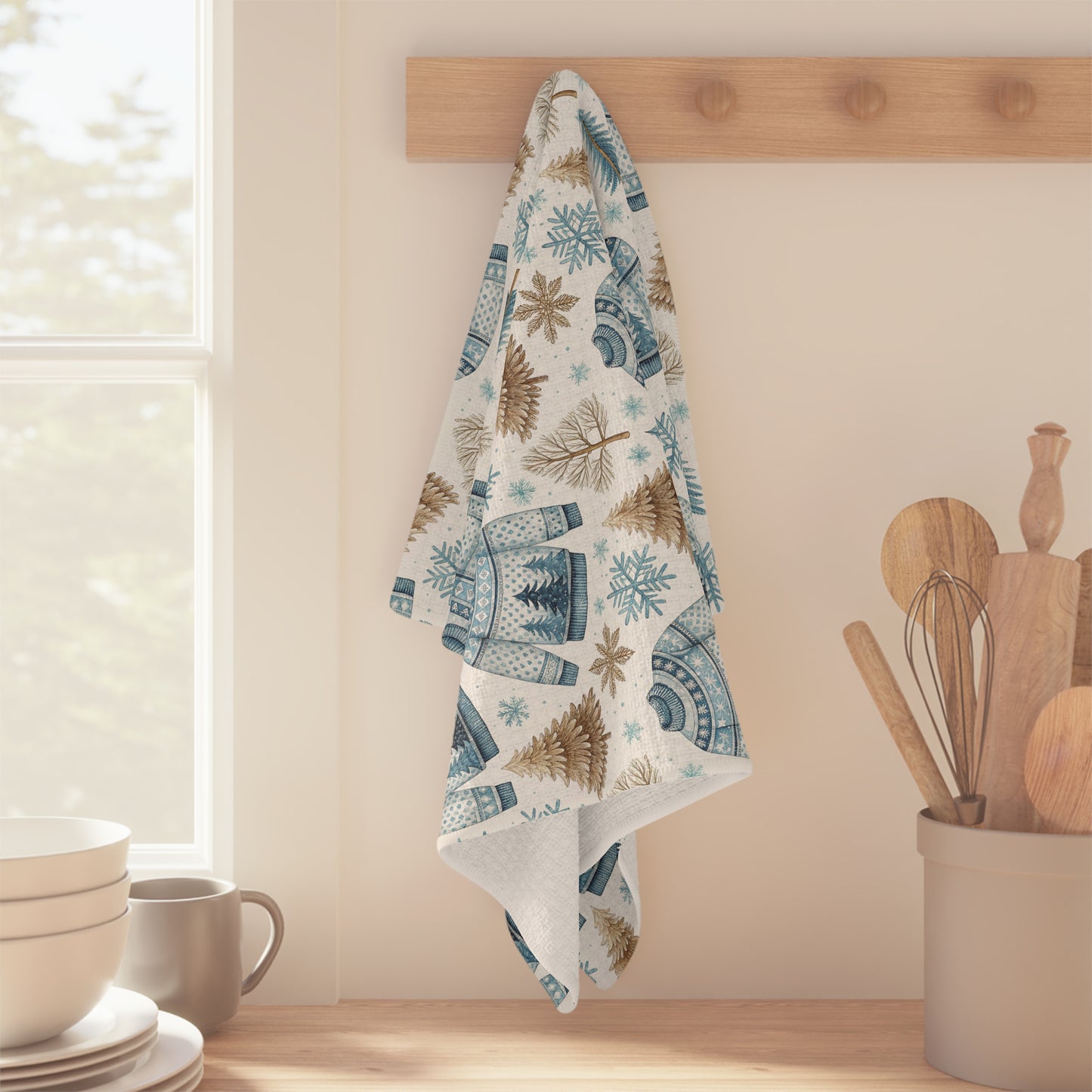 Nordic Fair Isle microfiber tea towel with blue sweaters, pine trees, and snowflakes, hanging on a wooden rack.