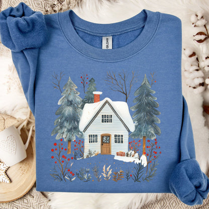 Indigo blue crewneck sweatshirt with a snowy cabin, pine trees, and red berries in a folk-art style.