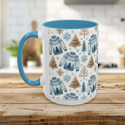 White ceramic mug with blue handle and interior, featuring a watercolor Nordic fair isle sweater, snowflake, and evergreen pattern.