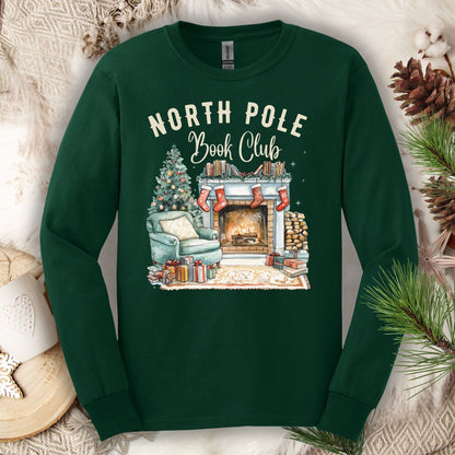 Forest Green Gildan long sleeve tee with "North Pole Book Club" text above a cozy fireplace, armchair, and Christmas tree scene.
