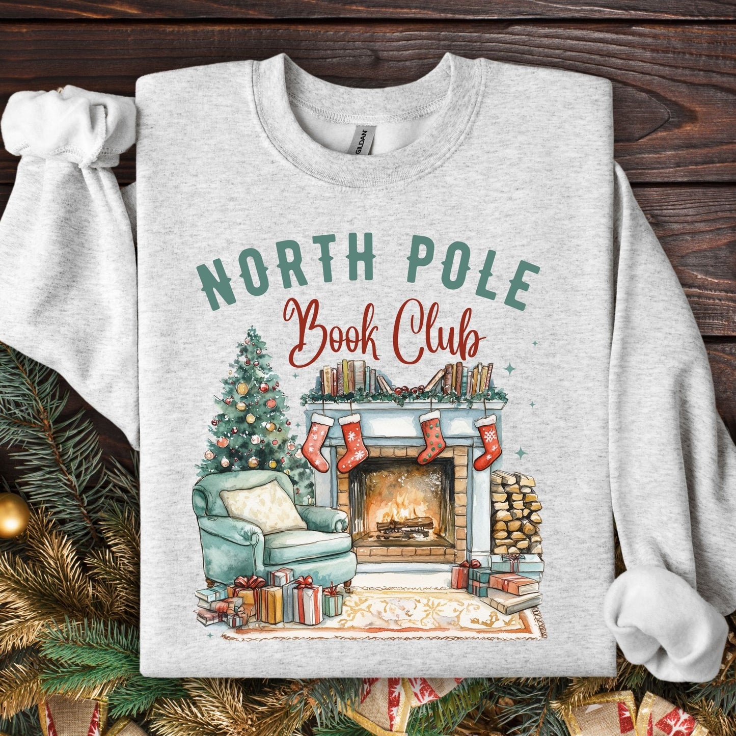 Ash Gildan sweatshirt with "North Pole Book Club" over a cozy fireside scene, Christmas tree, and books.