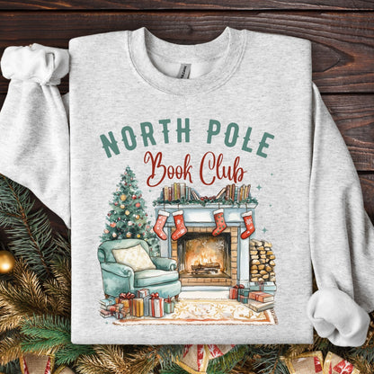 Ash Gildan sweatshirt with "North Pole Book Club" over a cozy fireside scene, Christmas tree, and books.