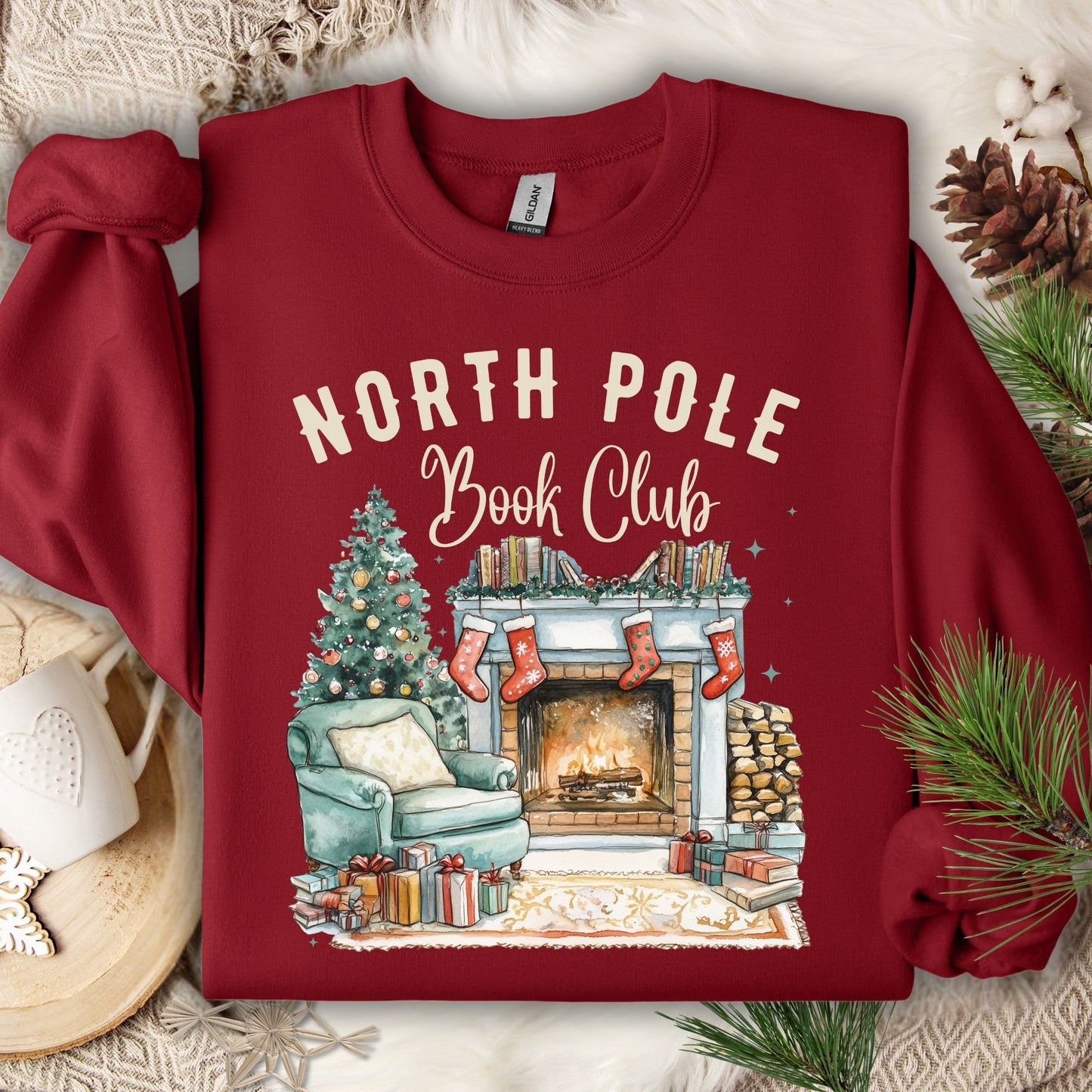 Cardinal Red Gildan sweatshirt with "North Pole Book Club" text and a cozy Christmas fireside scene.