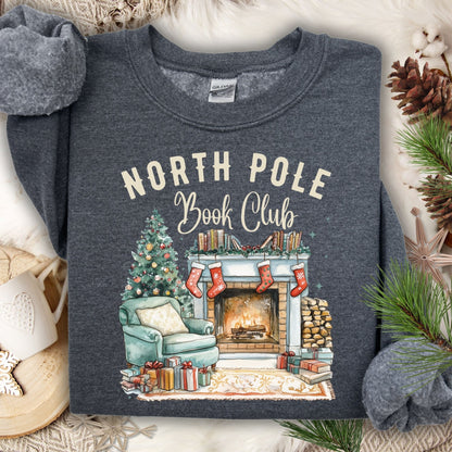 Dark Heather Gildan sweatshirt with "North Pole Book Club" text above a cozy Christmas fireplace scene.