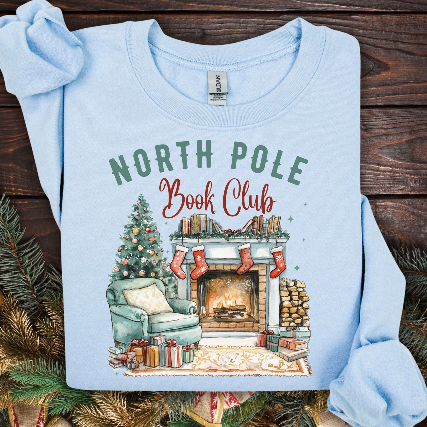 Light blue Gildan sweatshirt with "North Pole Book Club" text and a cozy Christmas fireplace scene.