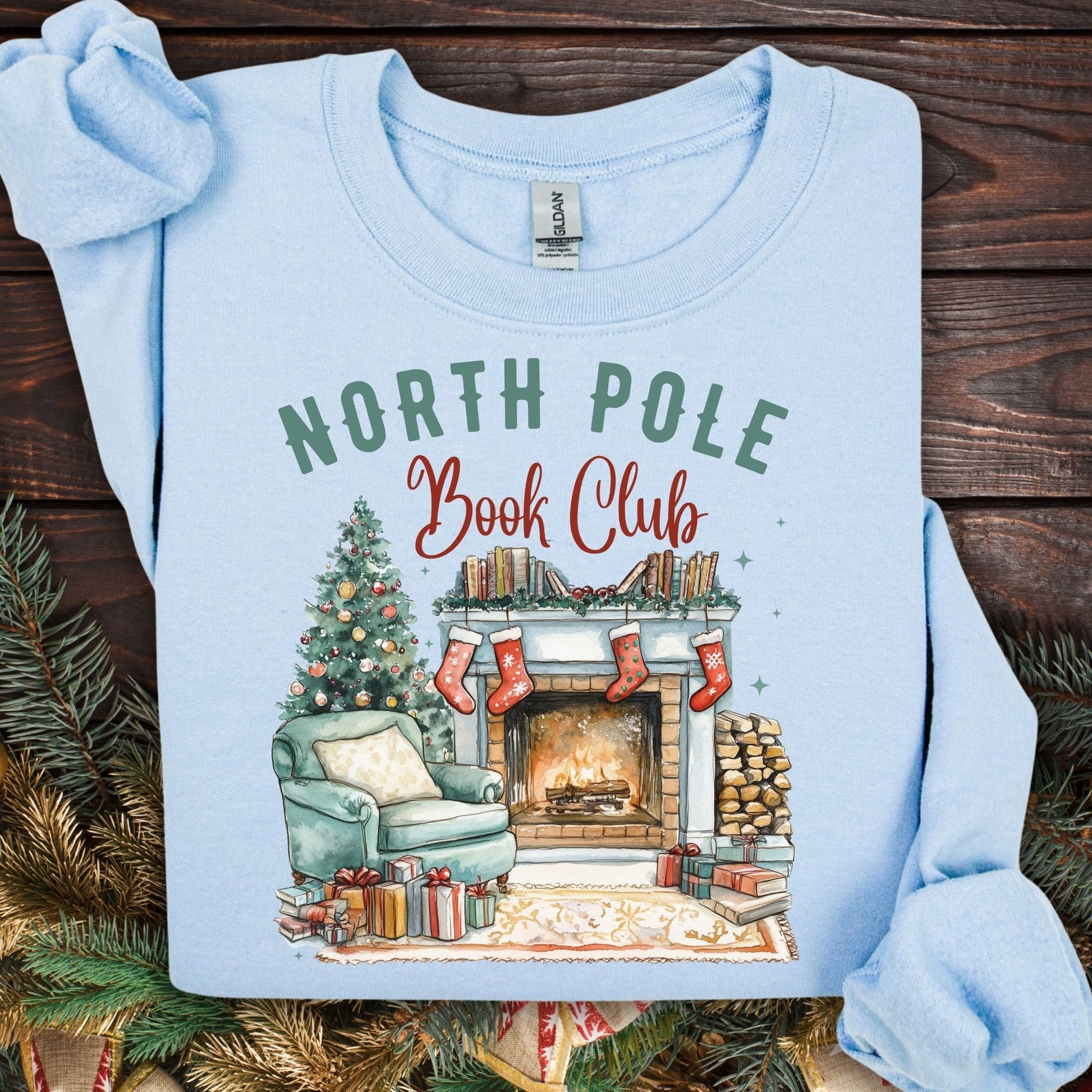 Light blue Gildan sweatshirt with "North Pole Book Club" text and a cozy Christmas fireplace scene.