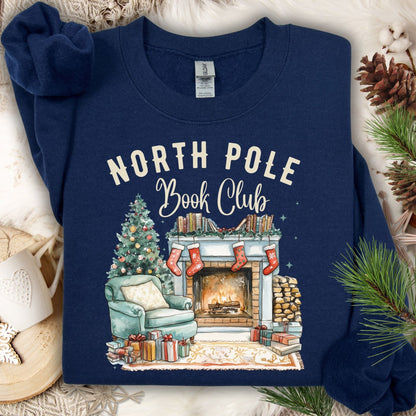 Navy Gildan sweatshirt with "North Pole Book Club" text and a cozy Christmas fireside scene.