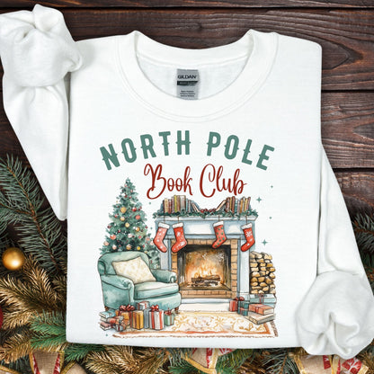 White Gildan sweatshirt with "North Pole Book Club" text and a cozy Christmas fireside scene.