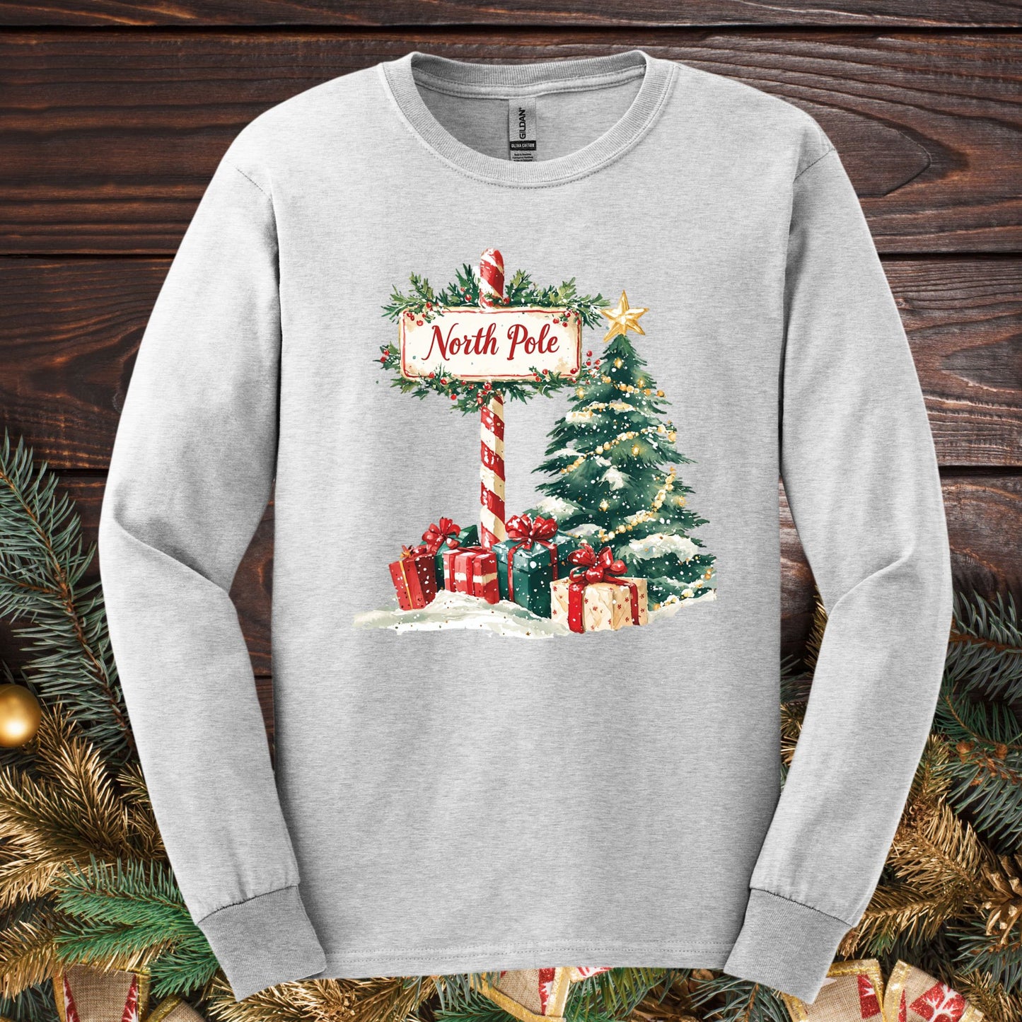 Ash long sleeve tee with a watercolor North Pole scene, gifts, and a glowing Christmas tree.