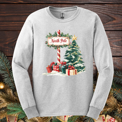Ash long sleeve tee with a watercolor North Pole scene, gifts, and a glowing Christmas tree.