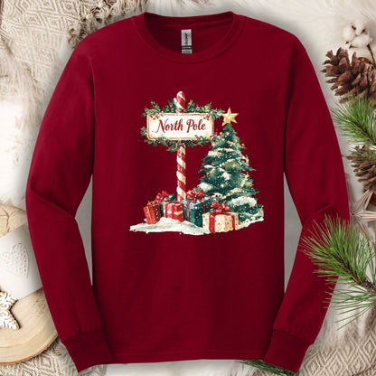 Cardinal Red long sleeve tee with a watercolor North Pole sign, snowy tree, and wrapped gifts.
