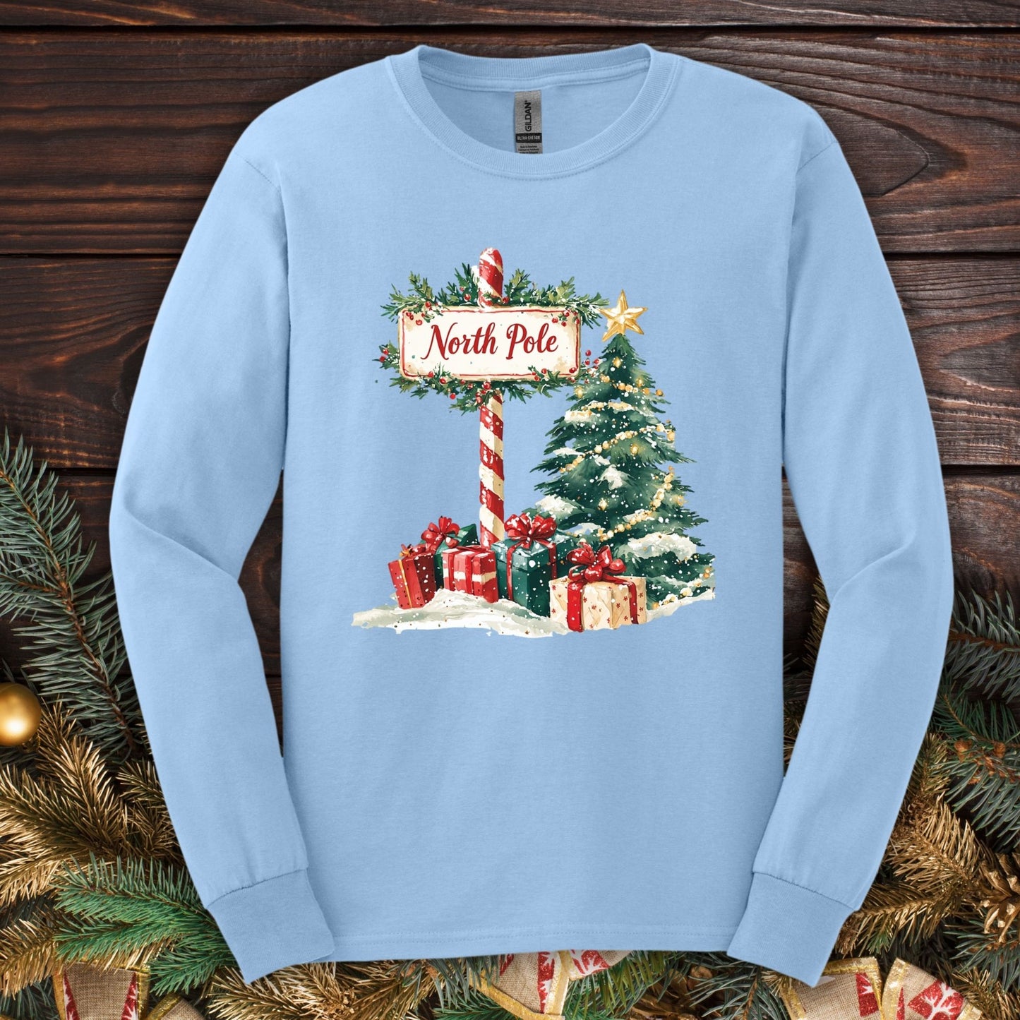 Light blue Gildan long sleeve tee with watercolor North Pole scene, gifts, and Christmas tree.