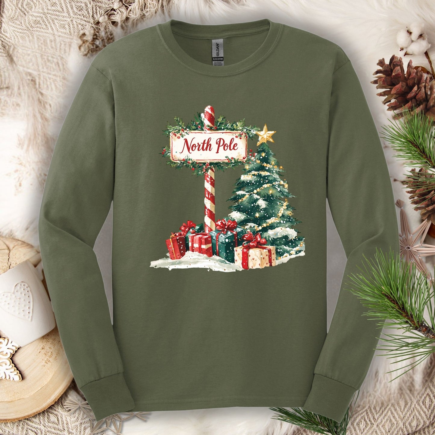 Military Green Gildan long sleeve tee with a watercolor North Pole sign, snowy tree, and gifts.