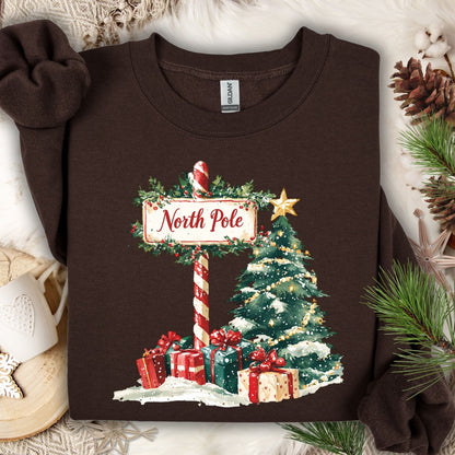 Dark Chocolate Gildan 18000 sweatshirt with a watercolor North Pole sign, snowy Christmas tree, and gifts.