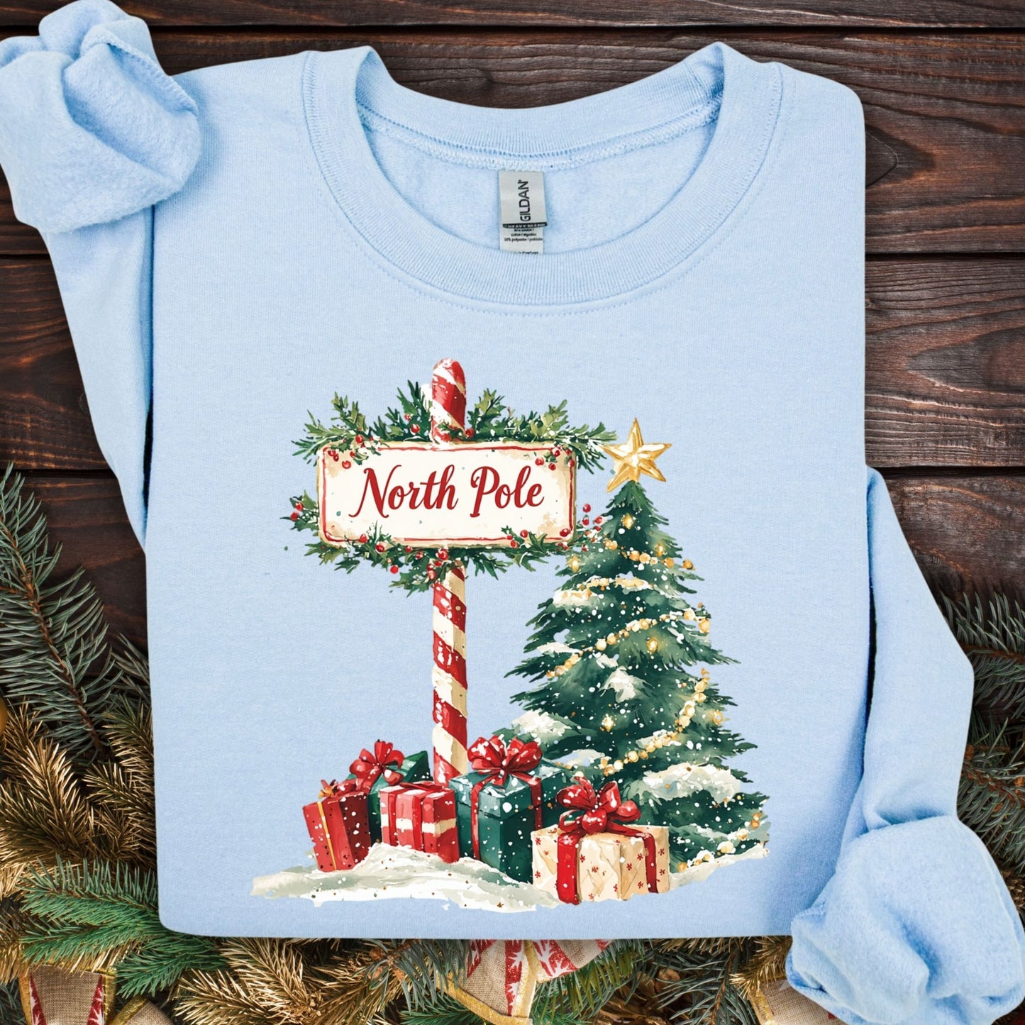 Light blue Gildan sweatshirt with a watercolor North Pole sign, Christmas tree, and gifts.