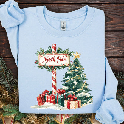 Light blue Gildan sweatshirt with a watercolor North Pole sign, Christmas tree, and gifts.