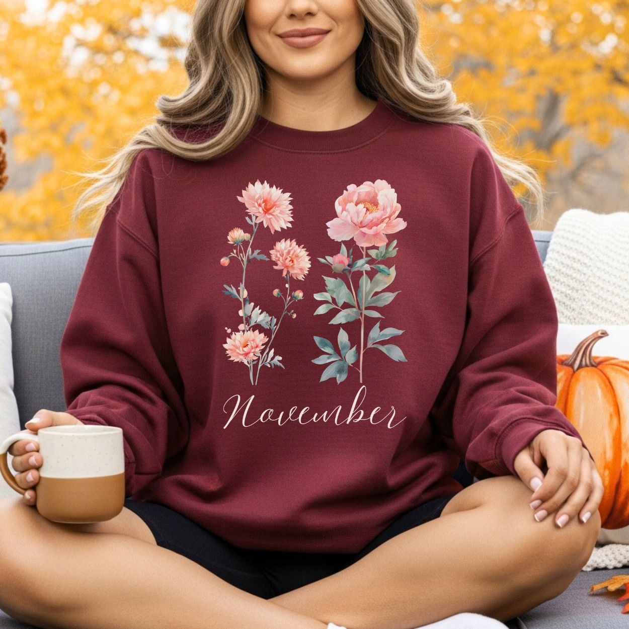 Maroon unisex sweatshirt with watercolor chrysanthemum and peony flowers, "November" text, worn by a woman outdoors.