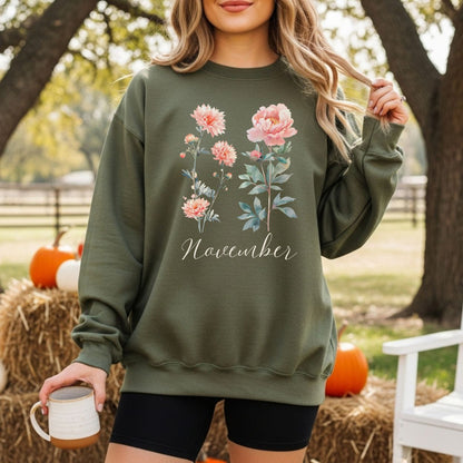 Olive green unisex sweatshirt with watercolor chrysanthemum and peony art, "November" script, worn outdoors.