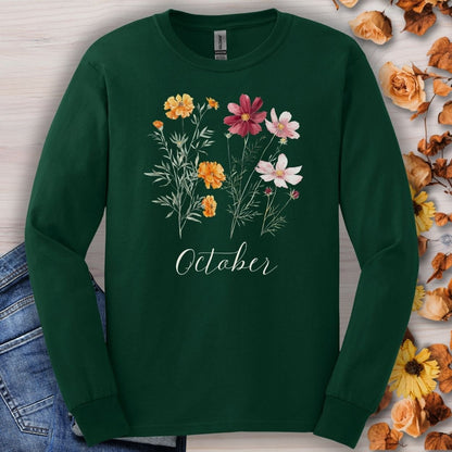 Forest Green long sleeve tee with watercolor marigolds, cosmos, and "October" text, styled with jeans and autumn leaves.